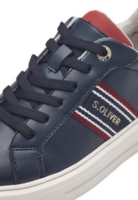 Sneaker in pelle blu navy con un accento rosso, strisce bianche e rosse e un logo dorato. Include lacci neri e una suola bianca texturizzata.
