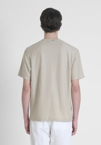 T-shirt beige a maniche corte, texture liscia, colletto rotondo, leggero lucido, presenta maniche raglan, branding minimale, vestibilità casual.