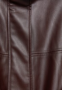 Matière en cuir marron foncé avec une texture de grain visible et des coutures verticales et horizontales.