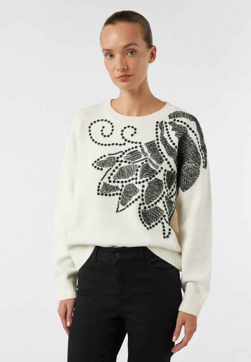 Biały sweter z czarnym wzorem liści oraz haftowanymi detalami. Sweter ma okrągły dekolt i ściągacze na rękawach.