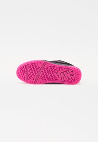 Semelle de chaussure avec une semelle crantée rose vif présentant un motif en losange et le logo "VANS" sur une chaussure noire sur fond blanc.