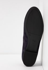 Chaussure en daim bleu marine foncé avec un bout rond, un dessus texturé et une semelle en caoutchouc noir lisse. Logo estampé sur la semelle.