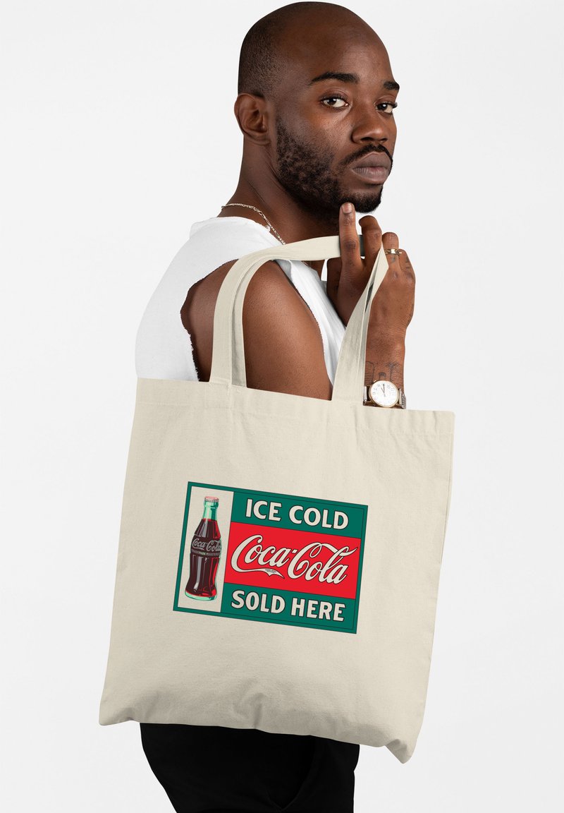 Borsa in tela beige con un design vintage della Coca-Cola. Presenta una bottiglia di vetro, accenti rossi e verdi, e un testo in caratteri in grassetto.
