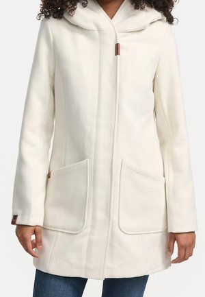 Mujer con un abrigo blanco con capucha, con grandes bolsillos frontales y detalles de botones marrones en las mangas y cerca del cuello.