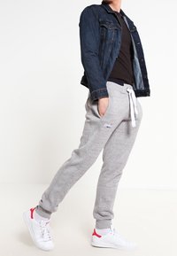 Graue Baumwoll-Jogginghosen mit elastischem Bund und weißem Kordelzug, kombiniert mit einer dunklen Jeansjacke und weißen Sneakers mit roten Akzenten.
