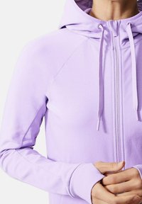 Sudadera con cremallera de color púrpura claro, fabricada en un tejido suave, con mangas raglán, capucha con cordones y puños acanalados para un ajuste ceñido.