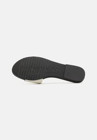 Semelle de chaussure en caoutchouc noir avec une texture côtelée et un accent blanc au talon. "CALVIN KLEIN JEANS" embossé sur la semelle intermédiaire. Pas de motifs visibles.