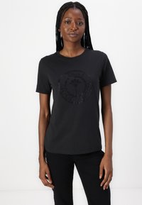 Black cotton t-shirt with short sleeves featuring a circular, textured design in black sequins at the center. Simple crew neckline, relaxed fit.