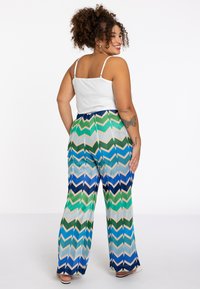 Witte tanktop en multicolored chevron-patronen brede broek met groen, blauw en marineblauw. Gladde textuur, losse pasvorm, hoge taille.