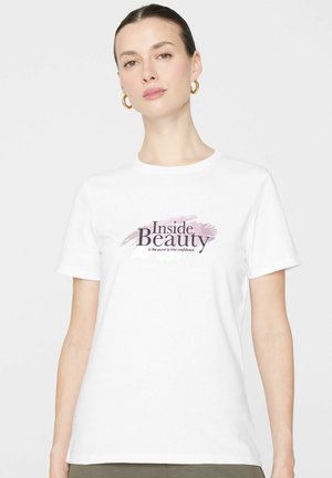 Mujer con el cabello recogido, llevando pendientes de aro dorados y una camiseta blanca con el texto "La belleza interior es el secreto para la verdadera confianza".