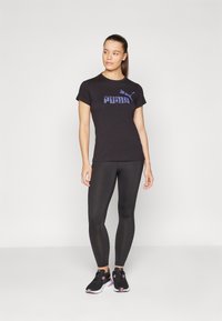 Svart kortermet t-skjorte med lilla Puma-logo, kombinert med svarte tights og svarte joggesko med pink detaljer.
