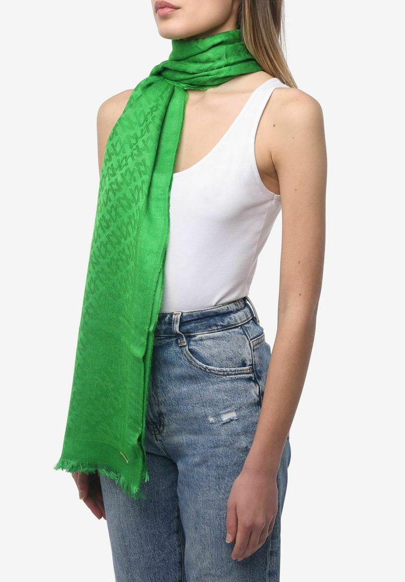 Groene sjaal gemaakt van een lichtgewicht materiaal, met een subtiel patroon, rafelige randen, en is om de nek van een persoon gewikkeld.