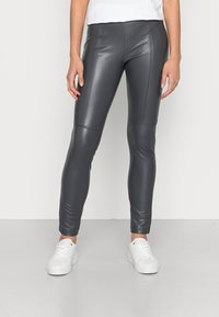 Grijze faux leren leggings met hoge taille, flatlock-naden, slanke pasvorm en een gladde textuur, gecombineerd met witte sneakers op een neutrale achtergrond.