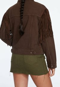 Bruine spijkerjasje met franjes aan de mouwen, voorzien van een aansluitende snit, verstelbare knopen en gecombineerd met een groene minirok.