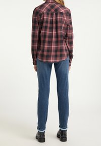 Svart och röd rutigt skjorta med långa ärmar, bakficka med detaljer, kombinerad med blå jeans och svarta skor. Synliga knäppta manschetter.