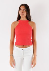 Top corto a halter rosso a coste con scollatura alta e spalle scoperte, abbinato a jeans bianchi a vita alta. Design semplice e aderente.