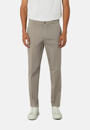 Pantalons beiges en tissu léger avec une fermeture à boutons à l'avant, dotés de poches latérales et d'une coupe droite. Portés avec des chaussures blanches.