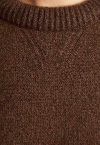 Gros plan d'un pull en laine brune tricoté avec col ras du cou côtelé et détail de couture en forme de V sous le col.