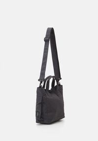 Musta kangaskassi, jossa on säädettävä olkahihna, kaksinkertaiset yläkahvat ja sivutasku logolla. Minimalistinen muotoilu ja suorakaiteen muotoinen.