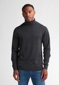 Jersey de cuello alto en gris oscuro, fabricado en un material de punto suave, con mangas largas y un dobladillo acanalado. Llevado con jeans azules.