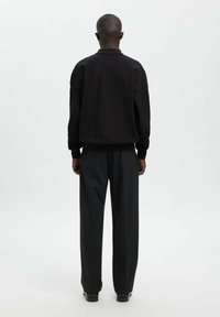 Czarna bawełniana bluza o luźnym kroju z ściągaczami przy rękawach, zestawiona z czarnymi spodniami o szerokich nogawkach wykonanymi z lekkiego materiału. Prosty, minimalistyczny design.