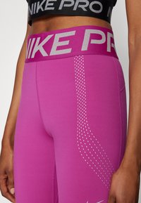 Nike Pro leggingai ryškiai rožiniai su plačiu elastingu juosmeniu. Yra atspindintis sidabrinis logotipas ir taškuotas raštas šonuose.