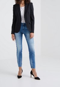 Černý tailored blazer přes bílý top, doplněný o světle modré skinny džíny a černé vysoké podpatky.