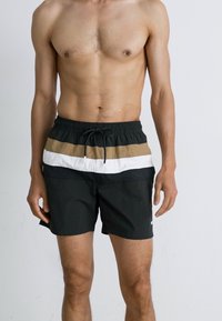 Schwarze Badeshorts mit einem Kordelzugbund, die horizontale Streifen in Beige und Weiß im oberen Bereich aufweisen. Leichter Stoff, lässiges Design.