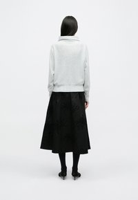 Γκρι, εφαρμοστό πουλόβερ με ψηλό γιακά, σε συνδυασμό με μια μαύρη φούστα που διαθέτει σύνθετο floral κέντημα και μπαίνει σε αχλάδι.