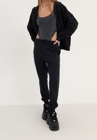 Felpa nera con cappuccio e zip, canotta grigia, pantaloni jogger neri con cordino e sneakers nere chunky; outfit atletico casual.