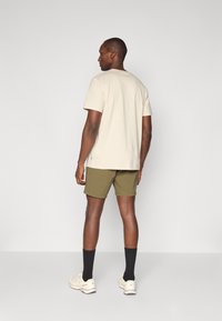 Tricou beige cu mânecă scurtă și pantaloni scurți verde măsliniu, purtați cu șosete negre și adidași deschiși, având un design simplu, fără modele.