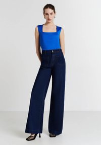 Top azzurro senza maniche con scollatura quadrata abbinato a jeans scuri di denim a vita alta e gamba larga. Scarpe con tacco in rete nera completano l'outfit.