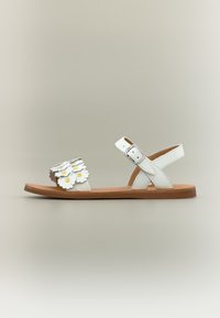 Sandale plate en cuir blanc avec sangle de cheville et boucle, décorée d'appliques de fleurs blanches et jaunes sur la bride avant.