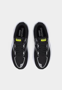 Ζευγάρι μαύρα αθλητικά παπούτσια New Balance με λευκές σόλες και ρευστερικές ασημί λεπτομέρειες, από πάνω, πάνω σε απλό φόντο.