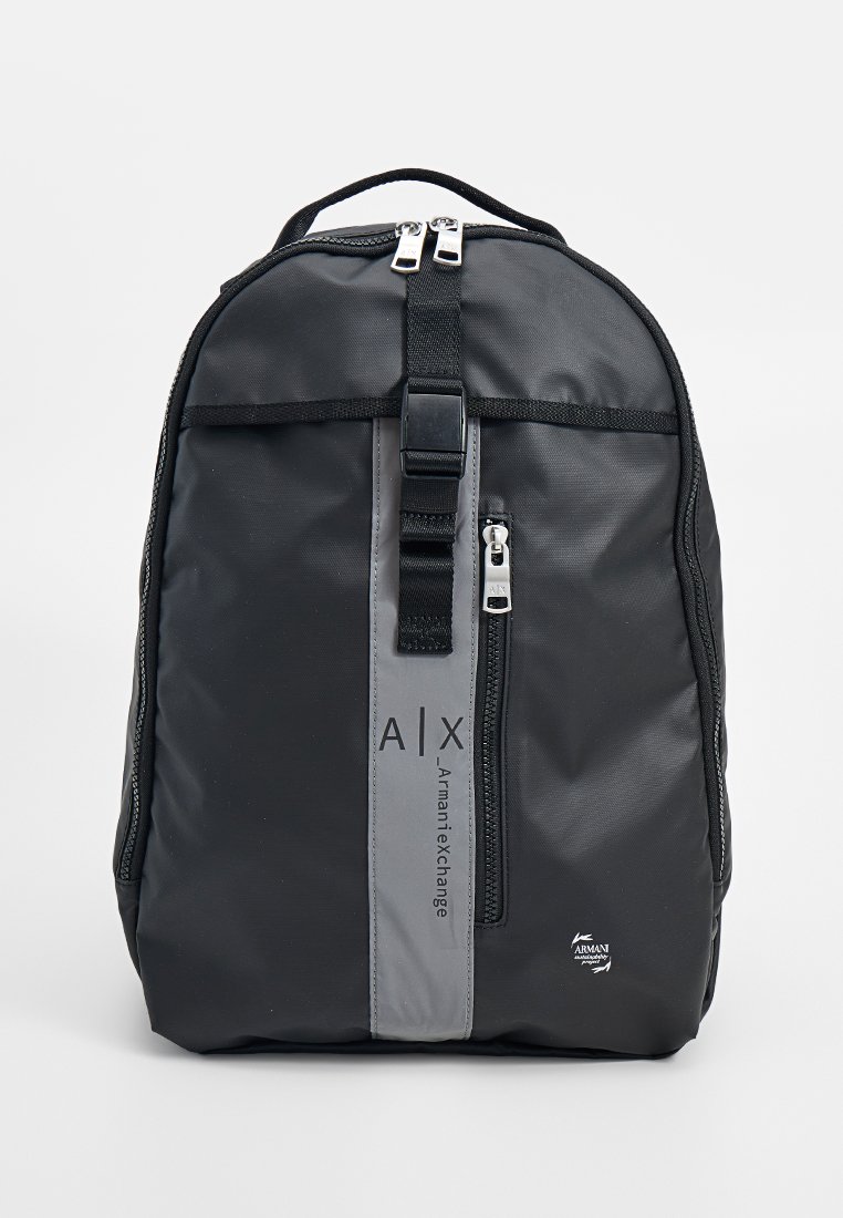 Sac à dos en nylon noir avec une bande grise, fermetures éclair doubles, bretelles réglables et détails de marque. Design compact et structuré.