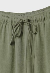 Pantalon en tissu vert olive avec taille élastique et lien noué au centre devant.