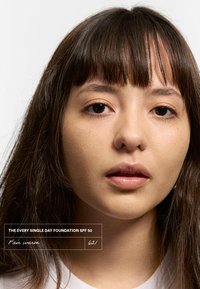 Fond de teint étiqueté "The Every Single Day Foundation SPF 50," teinte "Fair warm 621." Gros plan sur un visage avec une peau lisse, des cheveux bruns et un maquillage naturel.