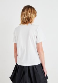 Witte katoenen t-shirt met korte mouwen, ronde hals en een relaxte pasvorm, gecombineerd met een zwarte rok. Focus op een eenvoudig design en textuur.