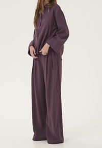 Set abbinato viola composto da una camicia morbida e ampia con bottoni e maniche lunghe, abbinata a pantaloni larghi, realizzati in un tessuto liscio e soffice.