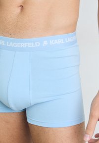 Fénykék boxer alsónadrág puha anyagból, fehér derékszíjjal, amelyen a "KARL LAGERFELD" felirat található. Simaság és testhez álló kialakítás jellemzi.