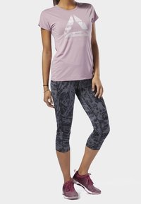 Světle fialová košile s krátkým rukávem a grafickým potiskem, kombinovaná s černými a šedými legínami 3/4 se vzorem a burgundskými sportovními botami.