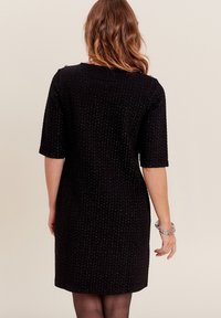 Robe noire en tissu texturé, à manches courtes et encolure ronde. Présente une coupe au genou et un motif subtil. Vue arrière montrée.