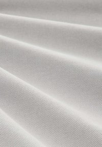 Close-up van glad, lichtgrijs stof met fijne diagonale weeftextuur en zachte, gelijkmatig verdeelde plooien.