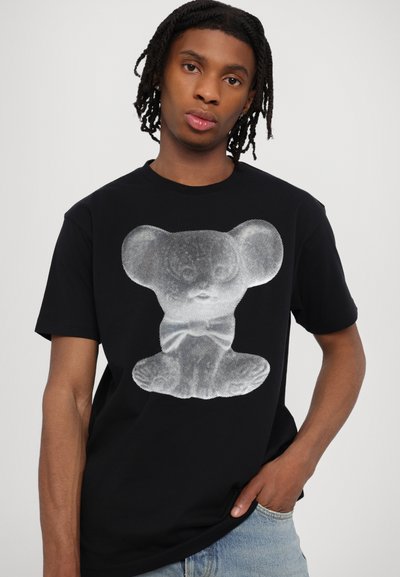 Black t-shirt featuring a large white graphic of a bear-like figure with oversized ears and a bow tie, made from cotton fabric.
