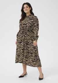 Langdurige mouw jurk in een beige en zwarte zebraprint, met een tailleband, knoopsluiting en een halflange zoom, gecombineerd met zwarte hakken.
