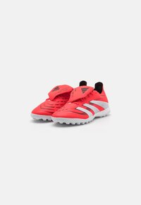 Red athletic shoes with mesh upper, white accents, and textured sole. Features a secure strap and contrasting logo on the tongue.
