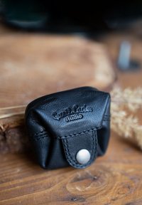 Schwarze Leder-Tasche mit strukturierter Oberfläche, ausgestattet mit einem Druckverschluss und geprägtem Branding. Kompakte Form mit gestickten Akzenten.