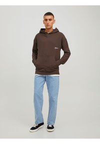 Haut à capuche marron en coton avec une poche avant et un petit logo. Associé à un jean en denim bleu clair et des baskets noires.