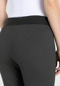 Schwarze Leggings im Hahnentritt-Muster mit einem breiten, strukturierten Bündchen. Der Stoff hat eine glatte Oberfläche, die das Zickzack-Muster hervorhebt.