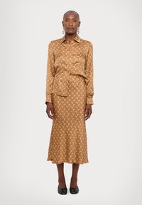 Brown satin shirt dress with crescent moon pattern, long sleeves, collared neck, semi-fitted design, flowing skirt, and black flats.